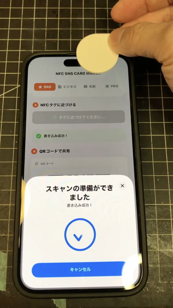 コイン型のNFCタグをiPhoneの上部に近づけているところ(実機)